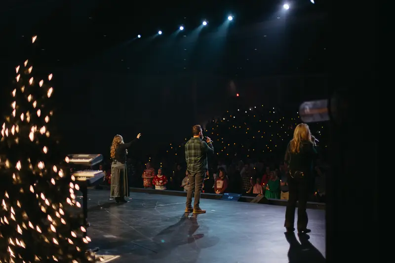 The worship team on stage beside a candlelit Christmas tree, with the congregation holding candles