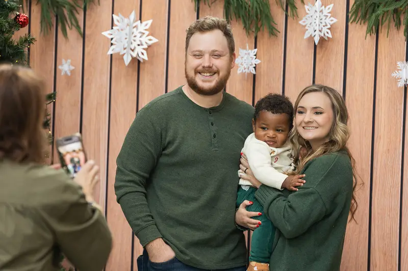 A family posing for a photo in front of a decorated wood-panel backdrop